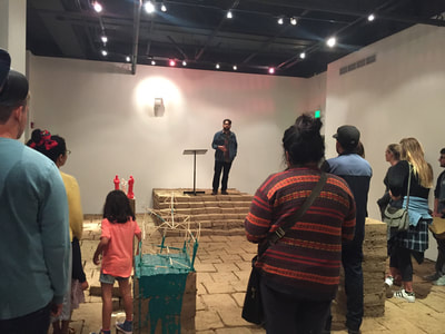 Photo of man reciting poetry on stage made of adobe bricks