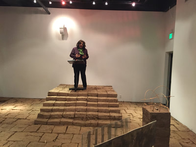 Photo of Tia Lucita performing a skit on stage made of stacked adobe bricks