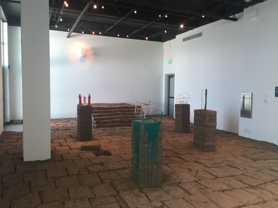 Photo of inside of gallery. Floor is covered in adobe bricks.