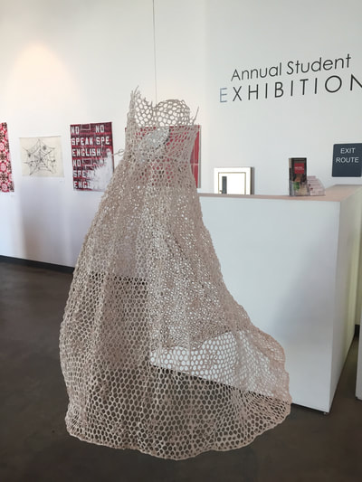 Picture of bridal style dress made from chicken wire and clay mixture hanging freely inside gallery.